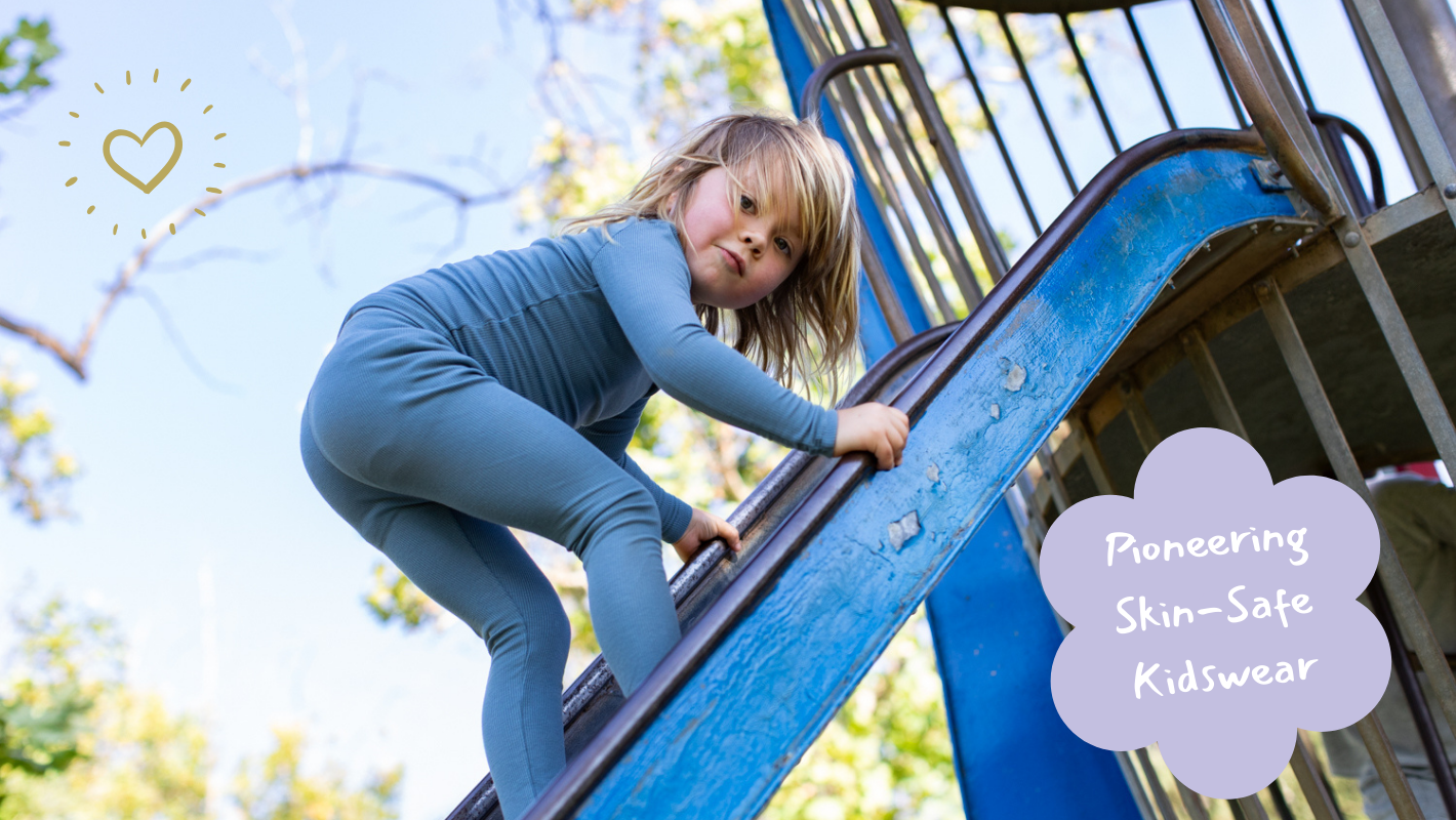 Child in blue leggings climbing a playground slide with 'Pioneering Skin-Safe Kidswear' text.